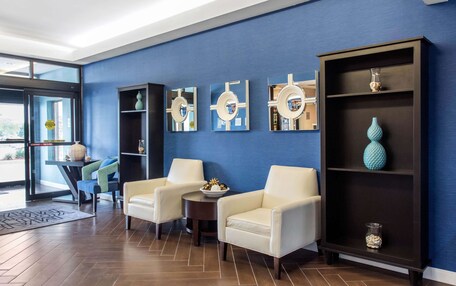 A modern lobby with two white armchairs, a round table, and a dark wooden bookshelf with decorative items.