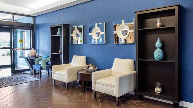 A modern lobby with two white armchairs, a round table, and a dark wooden bookshelf with decorative items. - Hampton Inn Douglas (Douglas)