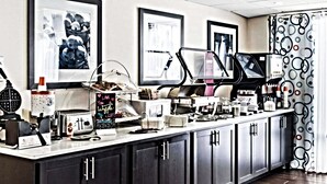 A breakfast area with a coffee machine, toaster, and waffle maker. There are framed pictures on the wall and a sign indicating the breakfast hours. - Hampton Inn Douglas (Douglas)