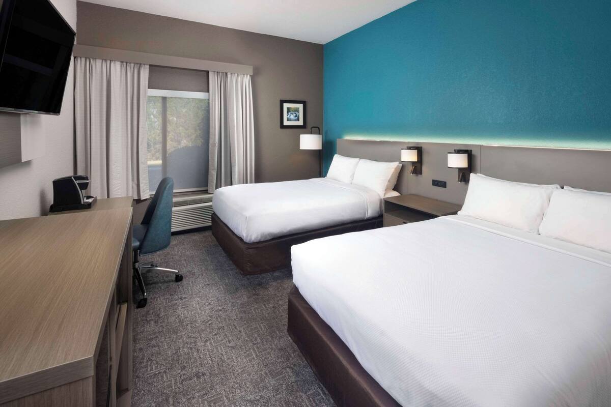 A hotel room with two beds, a desk, a chair, a TV, and a window with curtains.