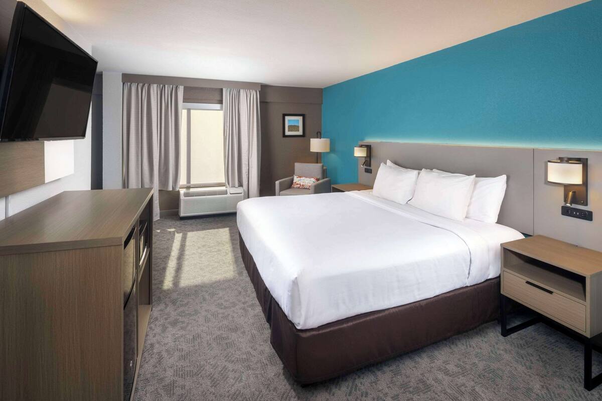 A hotel room with a large bed, a desk, a TV, and a window with curtains.