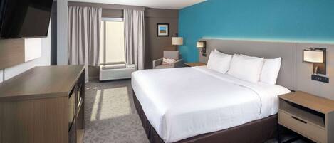 A hotel room with a large bed, a desk, a TV, and a window with curtains.
