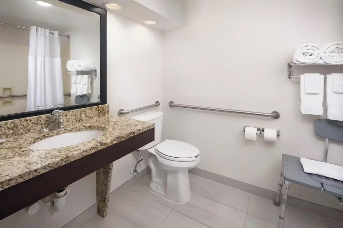 Un baño con encimera de granito, inodoro blanco, barandilla y perchero.