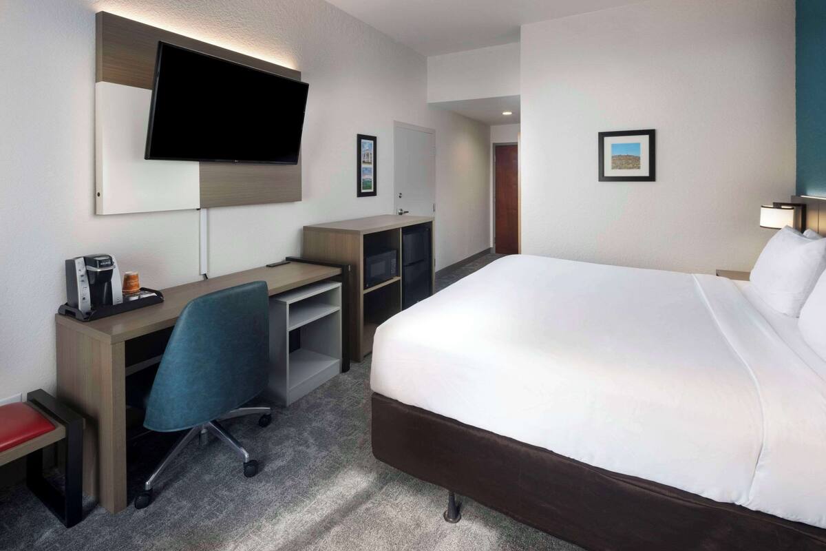 A hotel room with a bed, desk, chair, TV, and a coffee machine.