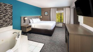 A hotel room with a bed, a large window with curtains, a TV mounted on the wall, a bathtub, and a wooden cabinet. - Comfort Inn & Suites Dahlonega University Area (Dahlonega)