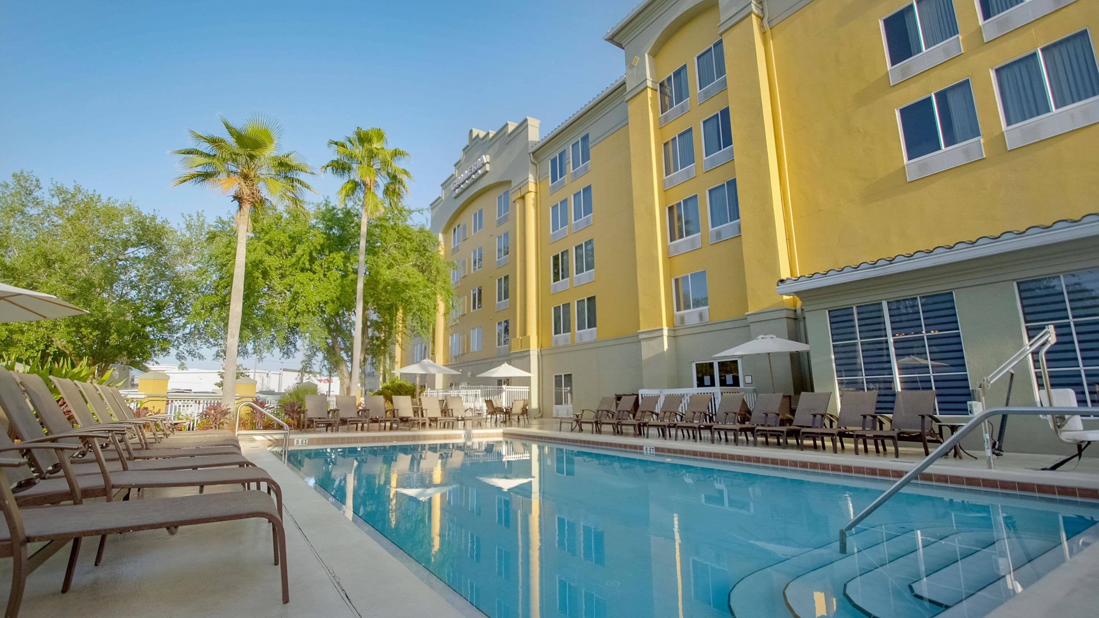 A pool area with lounge chairs and umbrellas, surrounded by a yellow building with multiple windows.