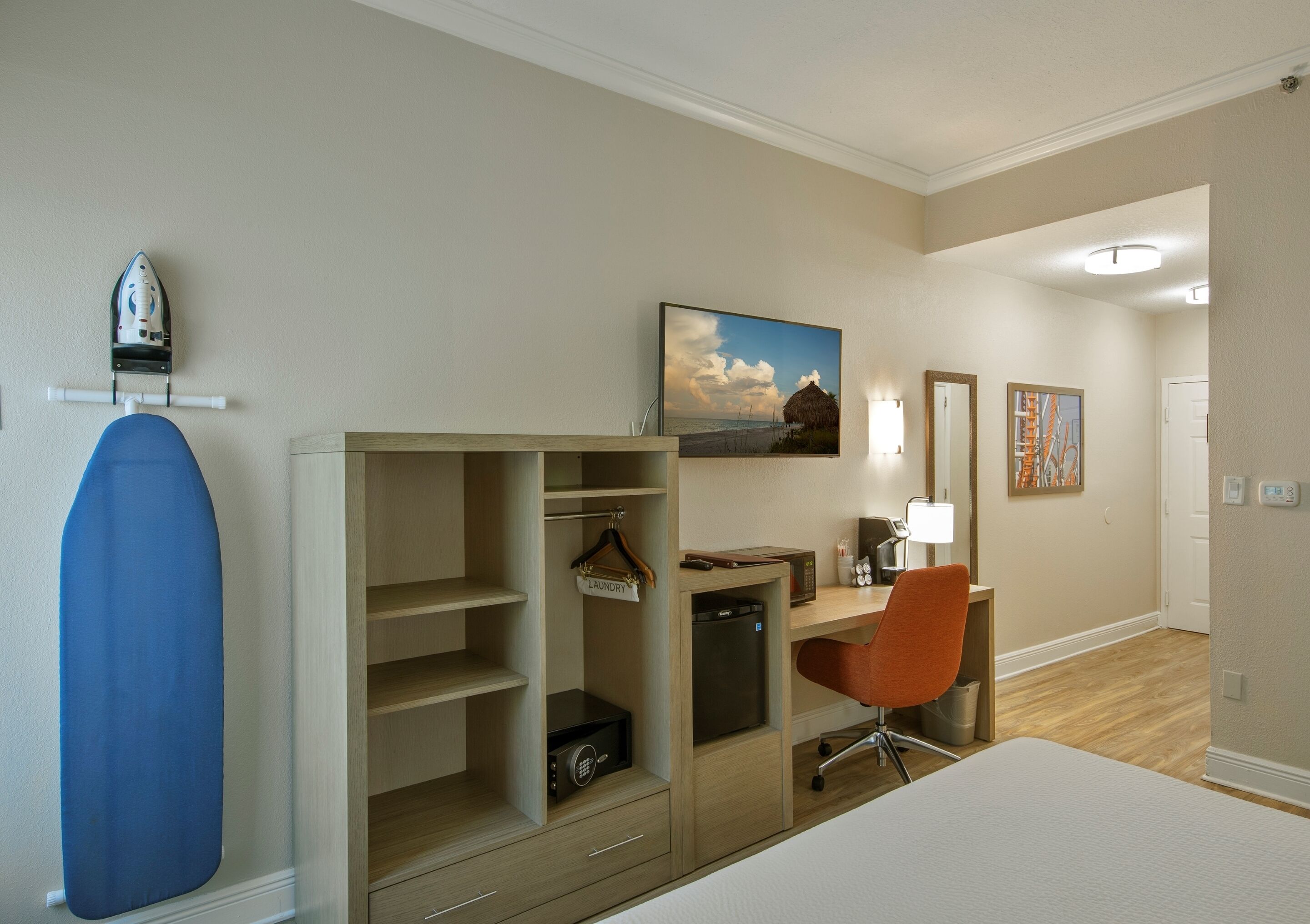 Un dormitorio con cama, escritorio, silla, armario y una plancha colgada.