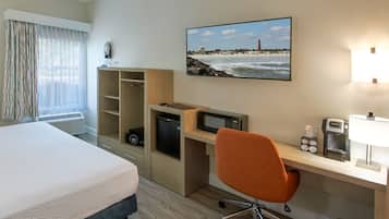 Una camera d'albergo con un letto, una scrivania con un computer, un forno a microonde e una macchina del caffè.