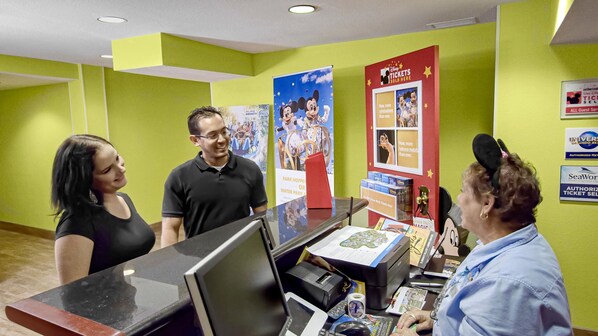 A reception desk with a computer, a ticket counter, and informational posters on the wall. - Galleria Palms Hotel (Kissimmee)