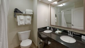 A bathroom with a toilet, two sinks, a mirror, and a towel rack with towels.