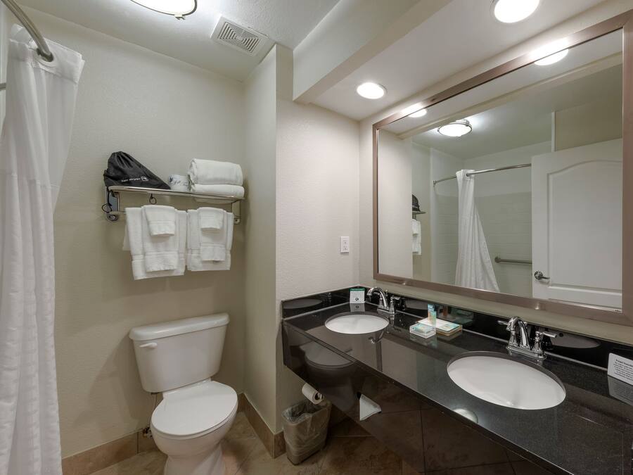 A bathroom with a toilet, two sinks, a mirror, and a towel rack with towels.