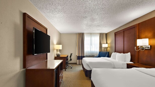 Habitación de hotel con dos camas, un escritorio, un televisor y una ventana con cortinas.