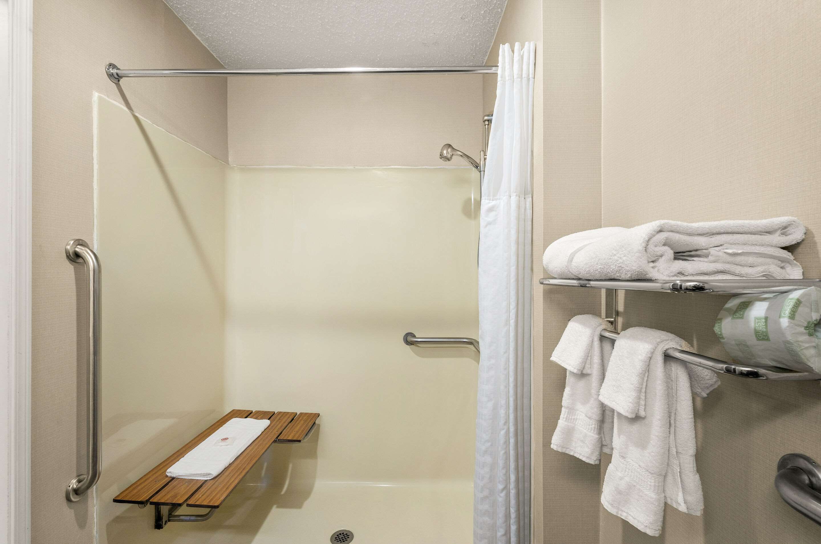 A shower area with a bench, grab bars, and a towel rack with towels.