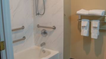 Ein Badezimmer mit barrierefreier Dusche, Haltegriffen, einer Badewanne und einem Handtuchhalter mit Handtüchern.