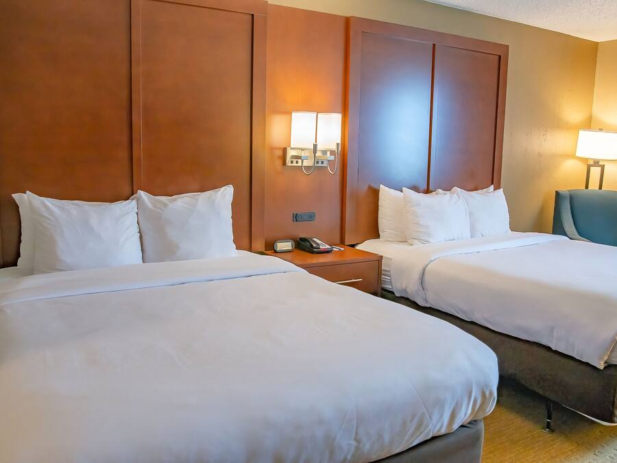 Quarto de hotel com duas camas, uma mesa de cabeceira com telefone e uma cadeira.