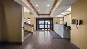 Un vestíbulo de hotel con suelo de madera, mostrador de recepción, teléfono y una escalera.