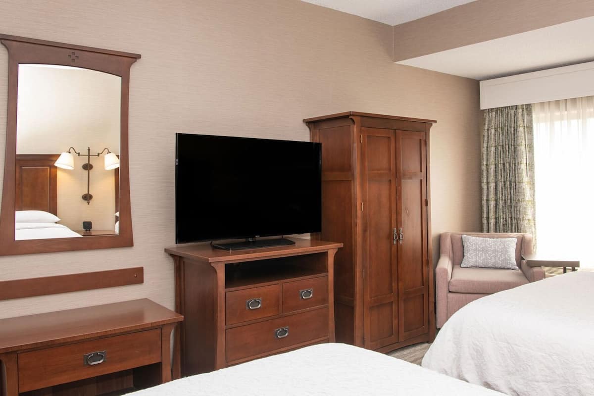 A hotel room with a bed, a TV, a wardrobe, a desk, and a chair.