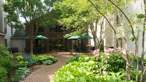A courtyard with a brick pathway, green benches, and potted plants. - Hampton Inn & Suites Rochester/Victor (Victor)
