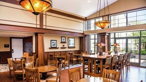 A spacious dining area with multiple wooden tables and chairs, large windows, and hanging lamps. - Hampton Inn & Suites Rochester/Victor (Victor)