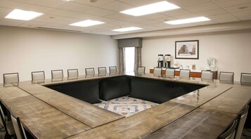 A conference room with a large oval table, chairs, a coffee station, and a framed picture on the wall.
