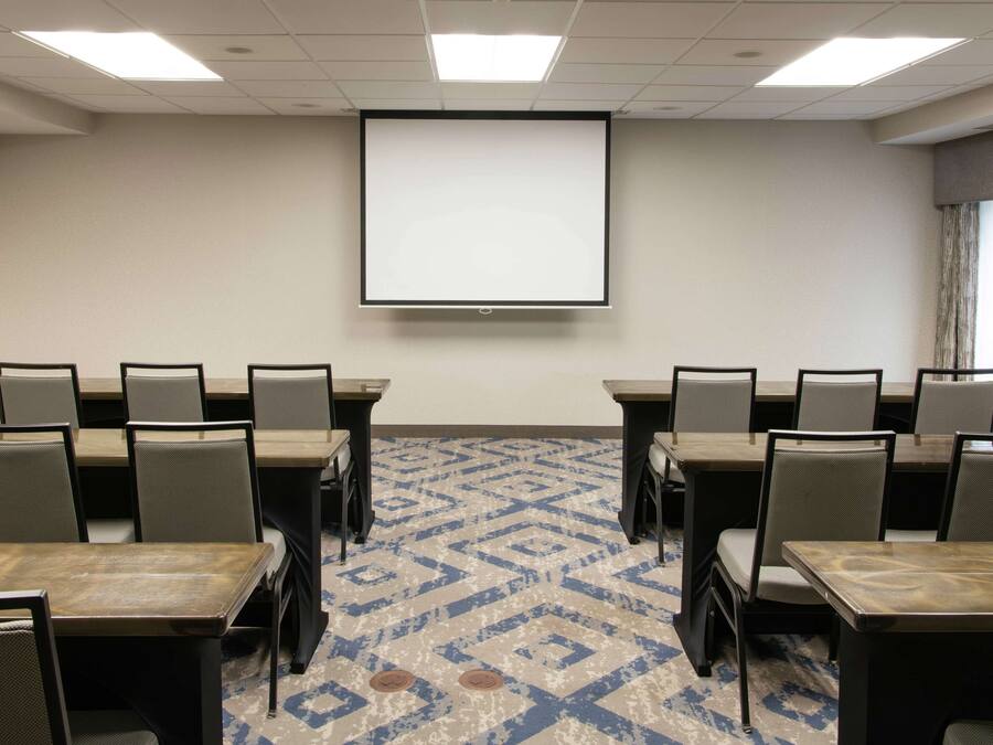 A conference room with a large screen, multiple tables, and chairs.