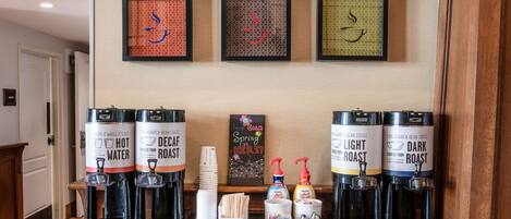 A coffee station with four coffee dispensers labeled 'Decaf Roast' and 'Light Roast', and a 'Dark Roast'. There are coffee cups and a 'Keep Calm' sign on the wall.