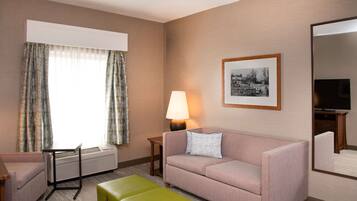 Habitación de hotel con sofá, mesa, lámpara, televisión y un cuadro en la pared.