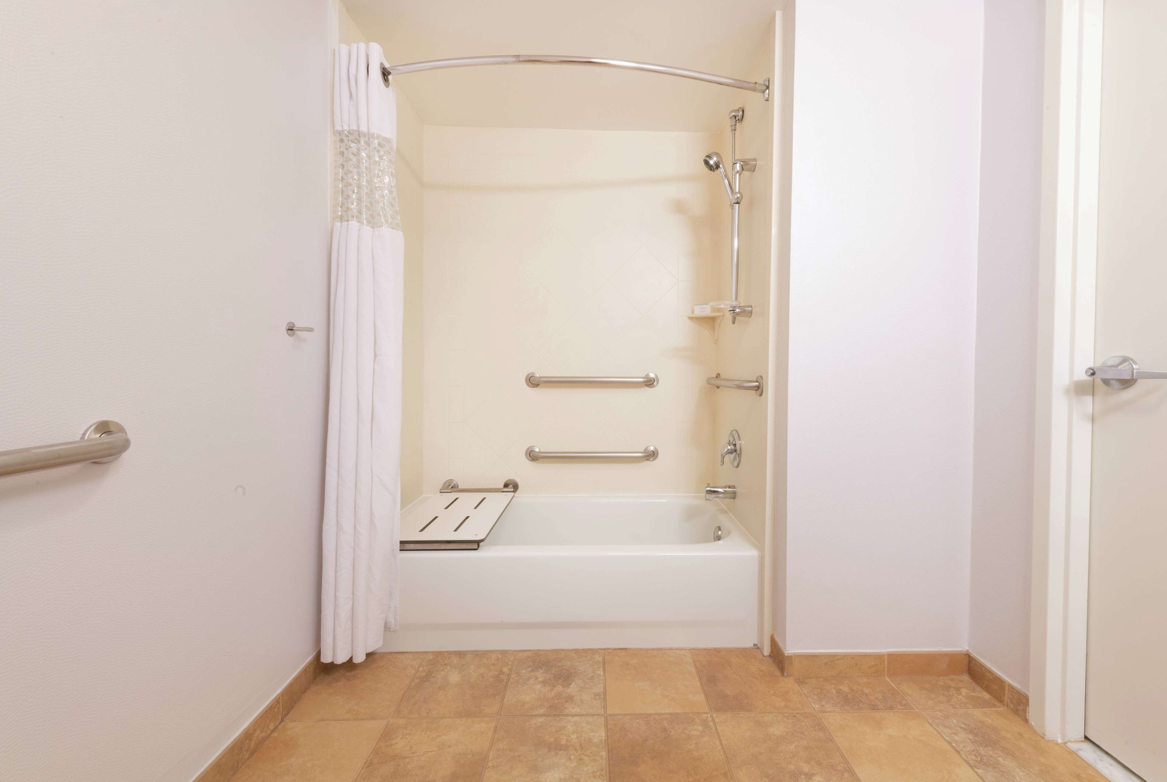 A bathroom with a shower, grab bars, and a white bathtub.