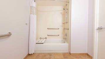 A bathroom with a shower, grab bars, and a white bathtub.