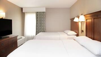 Habitación de hotel con dos camas, televisión, cómoda y ventana con cortinas.