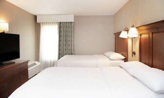 Habitación de hotel con dos camas, televisión, cómoda y ventana con cortinas.