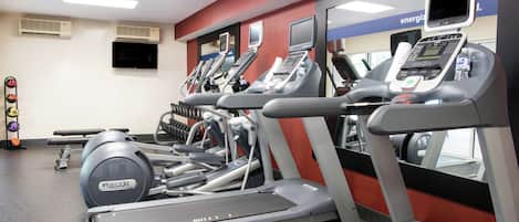 A gym with multiple treadmills, a wall-mounted TV, and a water bottle on one of the machines.