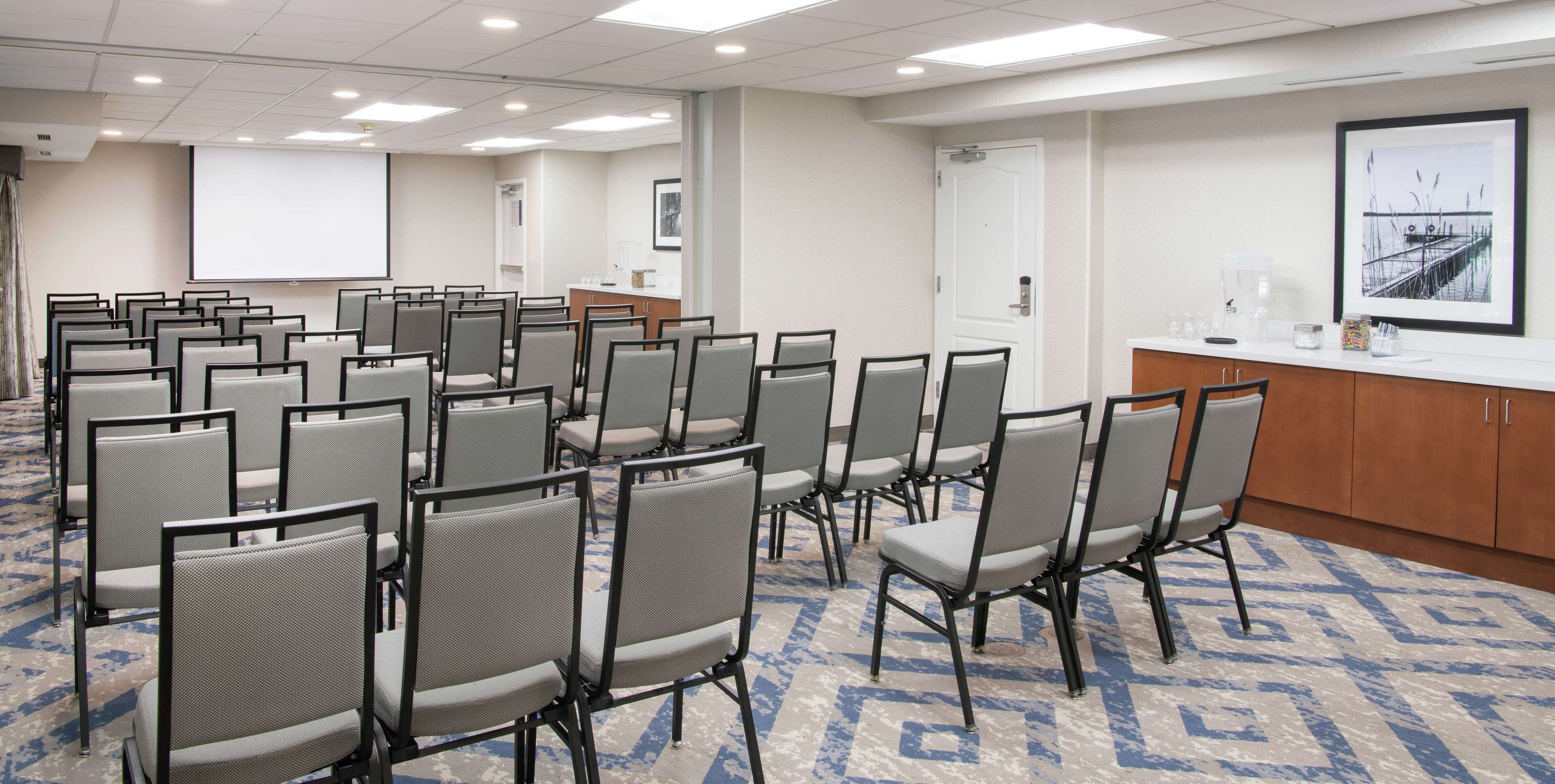 A conference room with rows of chairs, a projection screen, a podium, and a coffee station.