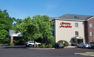 Edificio de Hampton Inn & Suites con entrada despejada, área de estacionamiento y un árbol grande al frente.