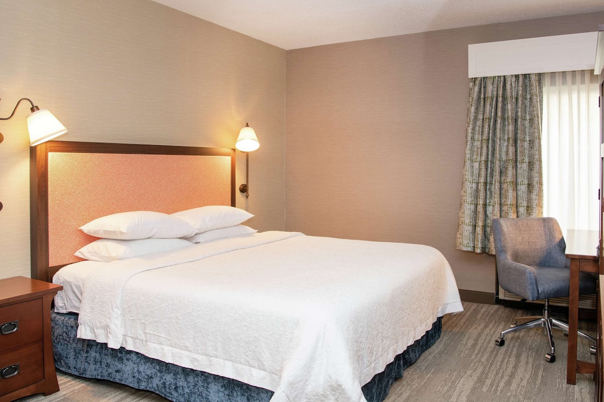 A hotel room with a bed, a desk, a chair, and a nightstand.