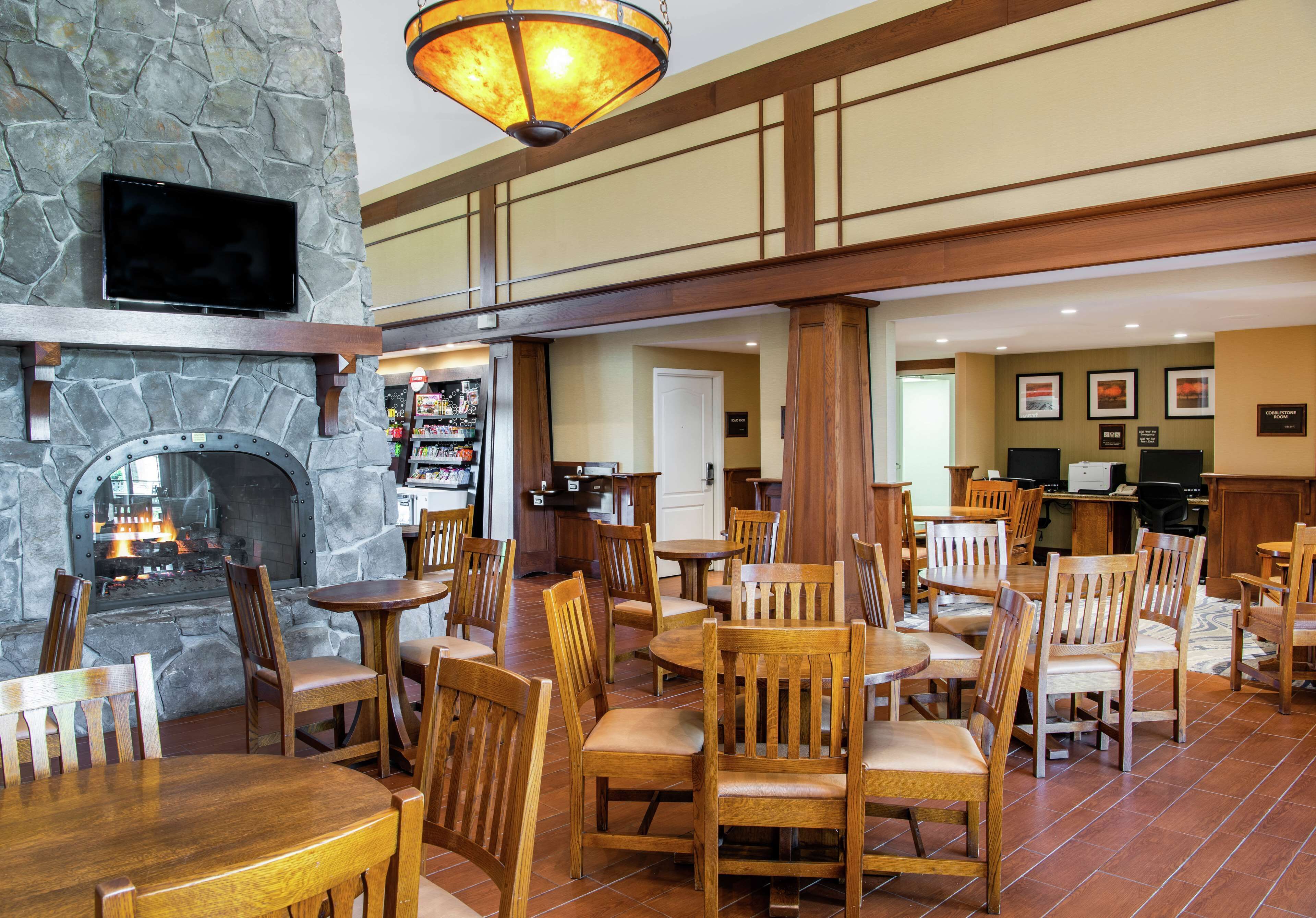 A restaurant with stone walls, wooden tables and chairs, a fireplace, and a television mounted on the wall.