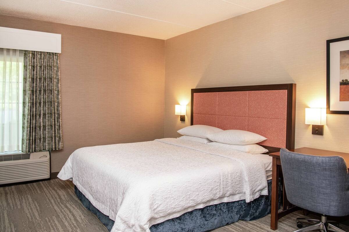 A hotel room with a bed, a chair, a desk, and a window with curtains.