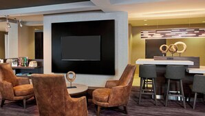 Een moderne hotel lobby met een groot flatscreen televisietoestel, comfortabele zitplaatsen, een bar en een decoratieve lamp.