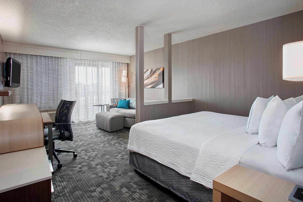 Een hotelkamer met een groot bed, een bureau, een stoel, een bank, een televisie en een lamp.
