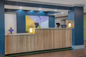 Un comptoir d’accueil d’hôtel au design moderne, doté d’un panneau frontal en bois, d’une grande œuvre d’art abstraite et d’un kiosque numérique.