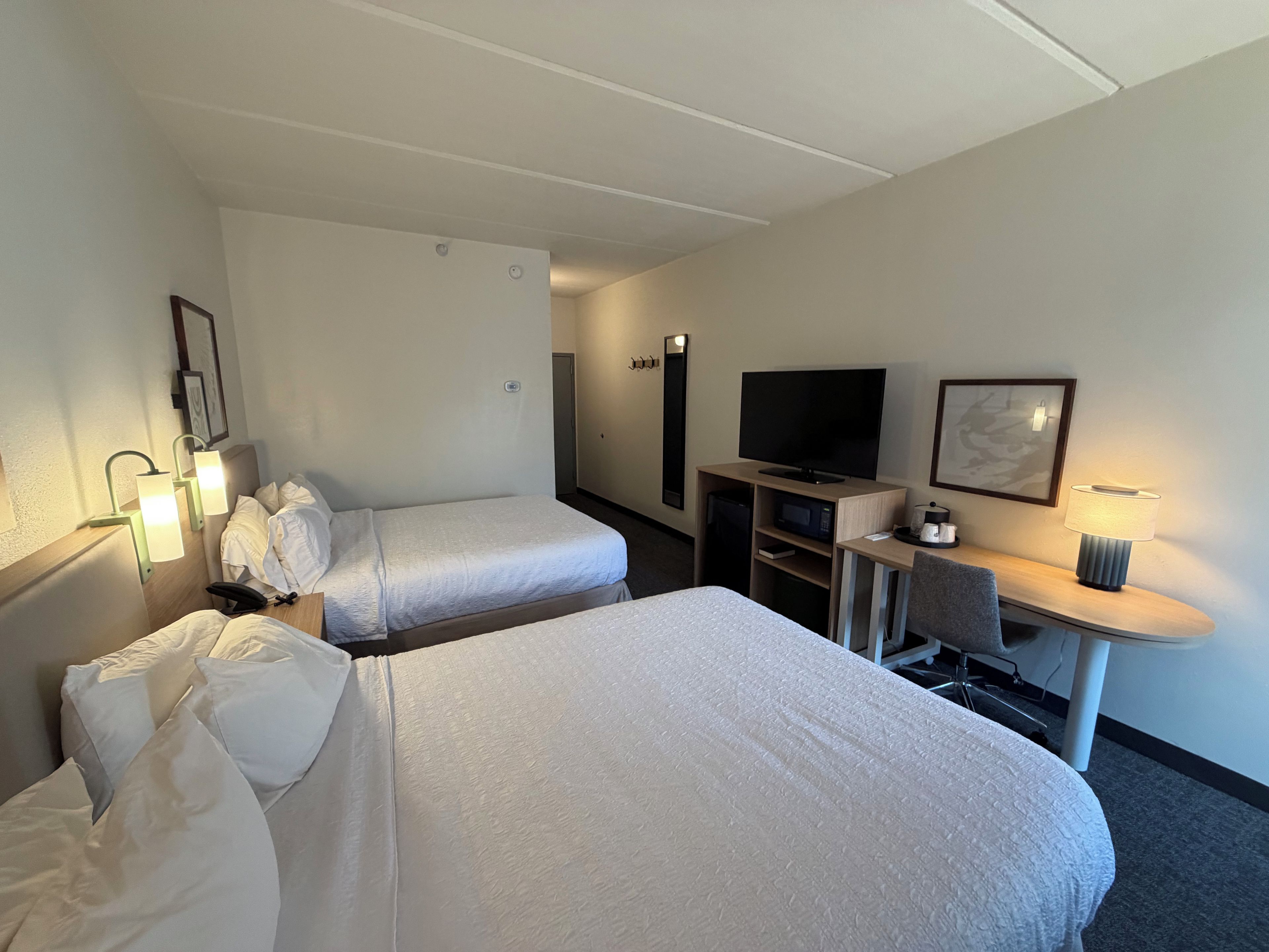 A hotel room with two beds, a TV, a desk with a lamp, and a microwave.