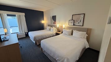 Habitación de hotel con dos camas, un escritorio, una lámpara y vista al mar.