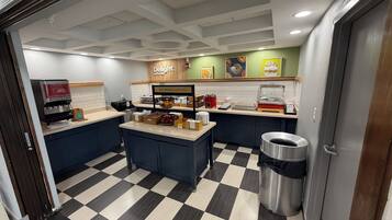 A breakfast area with a juice dispenser, a sign that says 'Delight in the day,' and a trash can.
