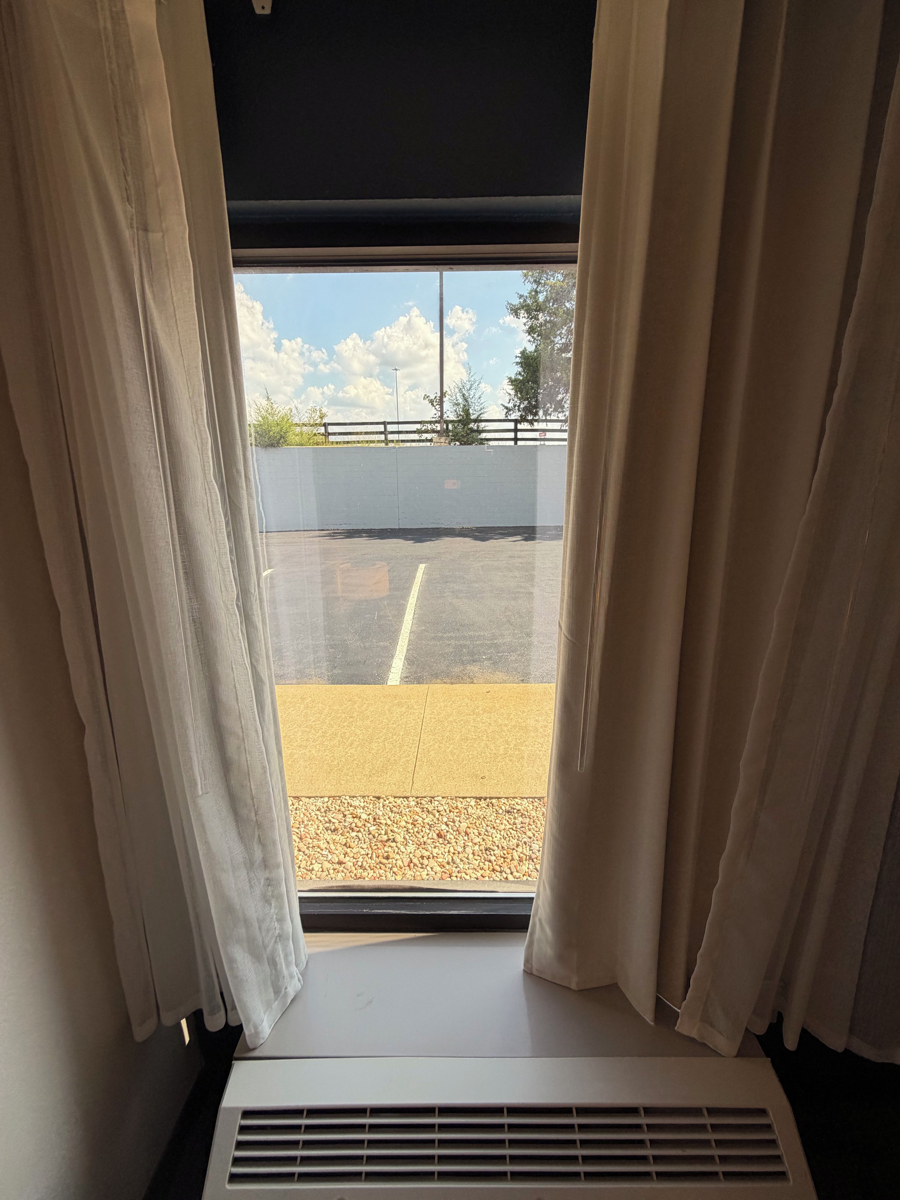 A window with curtains, a view of a parking lot, and a wall.