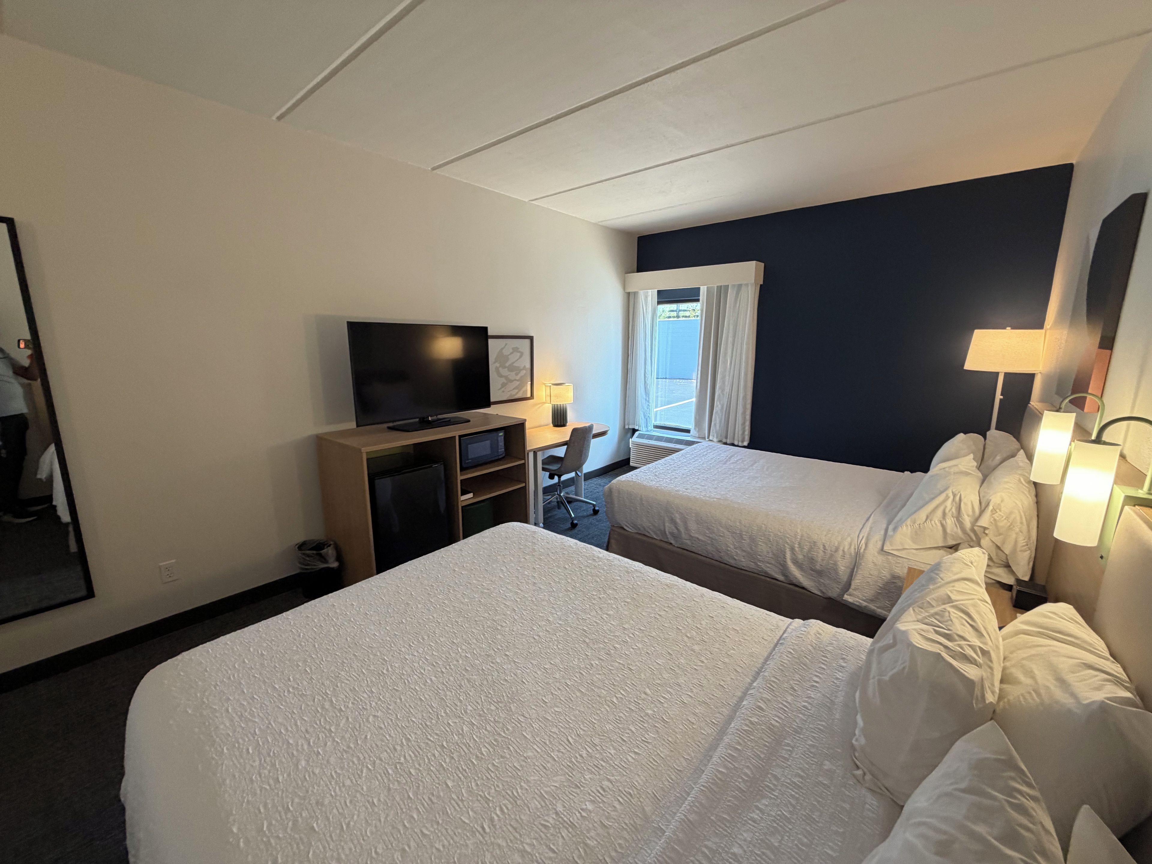 Habitación de hotel con dos camas, televisor, escritorio y ventana con cortinas.