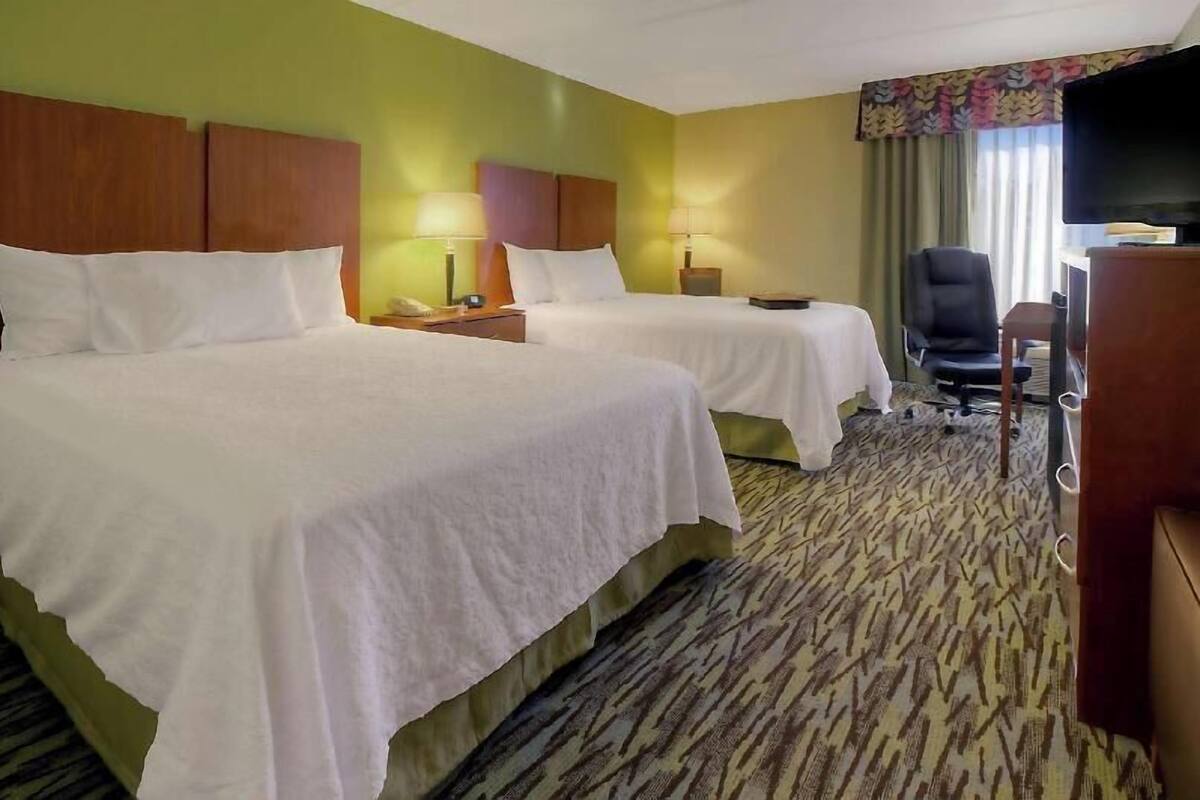 Ett hotellrum med två sängar, ett skrivbord, en stol, en tv och en mönstrad matta.