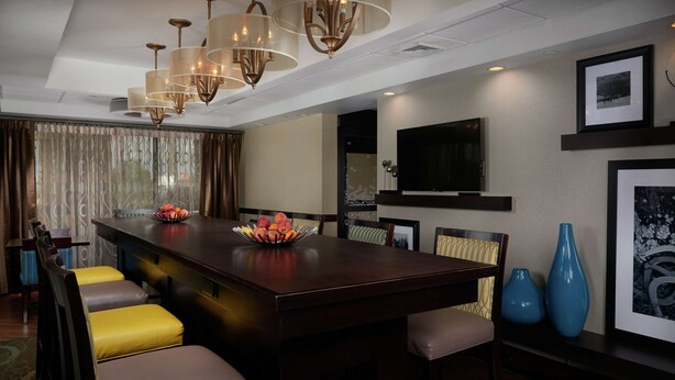 A modern hotel dining area with a central bar, cushioned seating, and a large TV on the wall. - Hampton Inn Franklin (Franklin)
