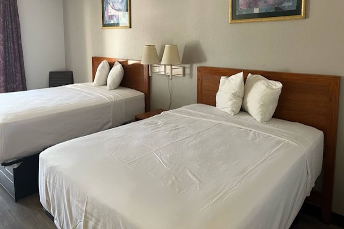Una habitación de hotel con dos camas, una mesita de noche, una lámpara y dos cuadros en la pared.