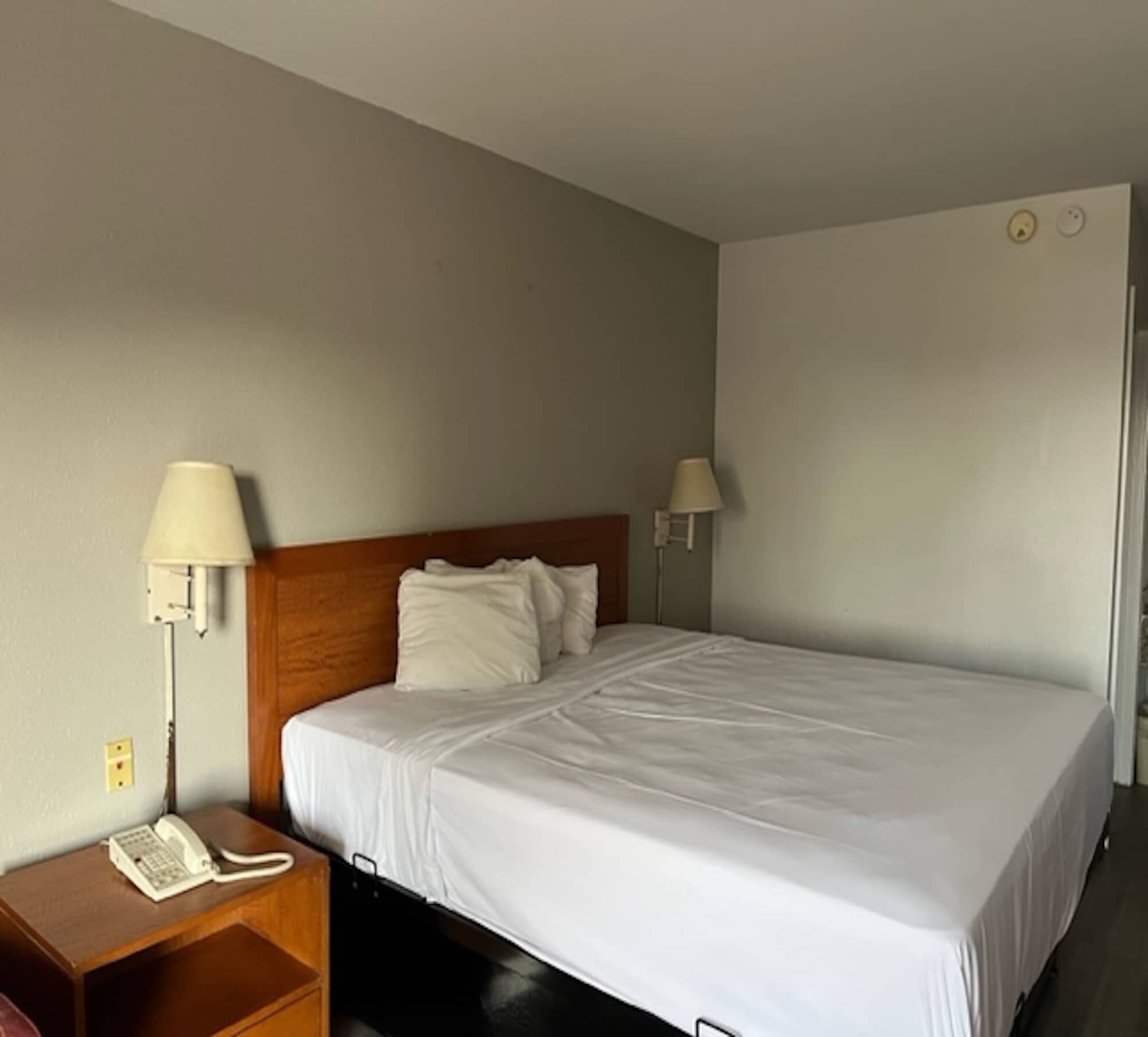 A hotel room with a single bed, a wooden nightstand with a telephone, and two wall-mounted lamps.