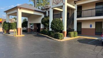 A hotel with a covered entrance, a parking lot, and a building with a balcony.